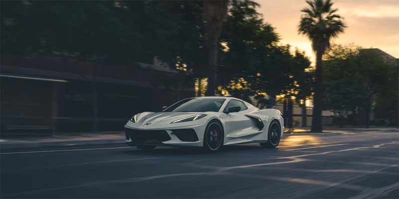 A white Chevrolet Corvette driving on a city street during sunset.